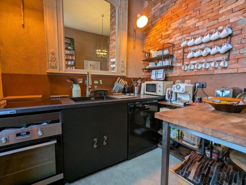 une cuisine avec des armoires noires et un mur en briques dans l'établissement Maison 10 pers. - Cour privative, Cinéma, Garage, Angoulême - FR-1-653-252, à Angoulême
