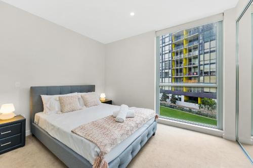 a bedroom with a bed and a large window at KOZYGURU MASCOT 2 BED Apt FREE PARKING NMA103 in Sydney