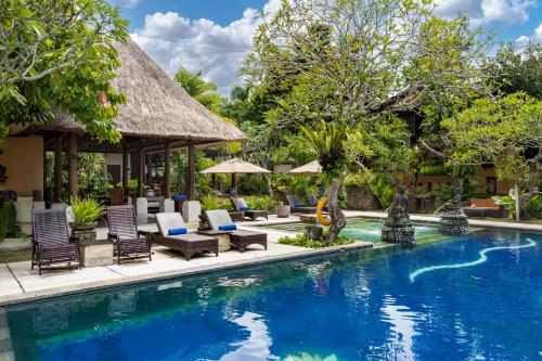 a pool at a resort with chairs and umbrellas at Svarga Bebek Villas in Ubud