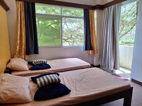 two beds in a room with two windows at Haven Haus with Mountain View in Baguio