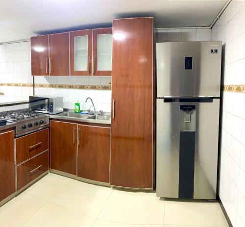 a kitchen with wooden cabinets and a stainless steel refrigerator at EmbajadaUsacorferiasAeropuertoG12Agora in Bogotá