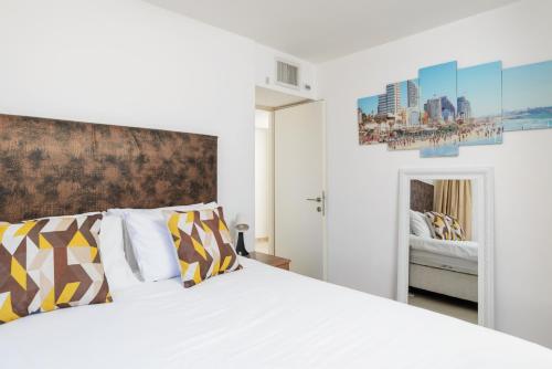um quarto com uma cama branca com almofadas amarelas e cinzentas em Penthouse with Panoramic View by FeelHome em Tel Aviv