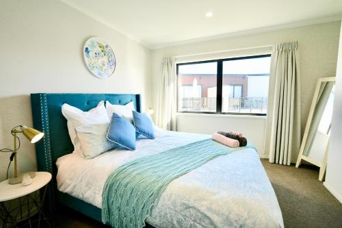 a bedroom with a bed with blue pillows and a window at Two-Bedroom House with Jacuzzi at Rototuna! in Hamilton