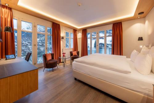 una camera d'albergo con letto, scrivania e finestre di Belvedere Swiss Quality Hotel a Grindelwald