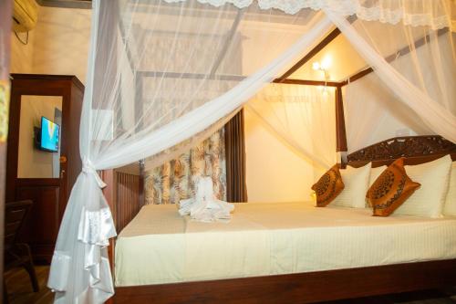 a bedroom with a canopy bed with white curtains at Ranagiri Relaxing Bungalow in Bentota