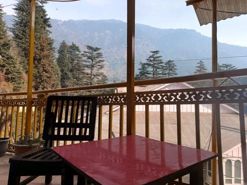 un tavolo rosso e una sedia sul balcone con vista di iSaint's Kuteer a Manāli