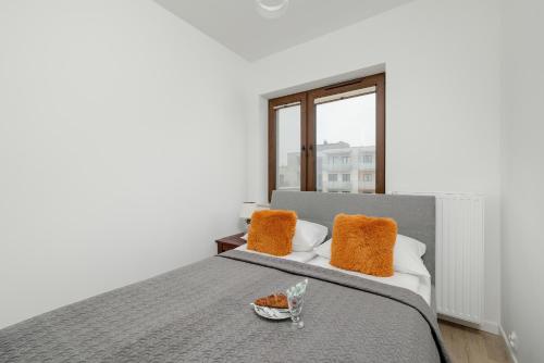 a white bedroom with a bed with orange pillows at Modern Apartment 1 Maja with Parking in Kołobrzeg by Rent like home in Kołobrzeg