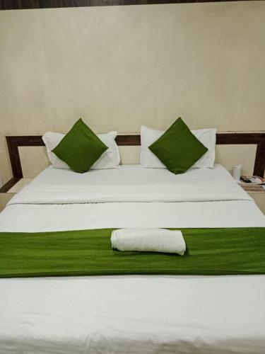 a white bed with green pillows and a towel on it at Hotel Cozy Residency in Jabalpur