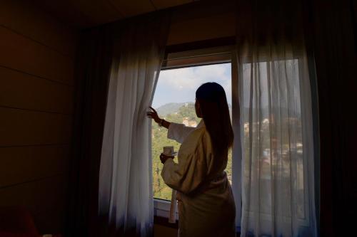 a woman is looking out of a window at Super Hotel by Perfectstayz Mall Road in Mussoorie