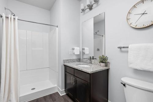 uma casa de banho com um lavatório, um chuveiro e um relógio. em CozySuites Nora 2BR next to Whole Foods em Indianápolis