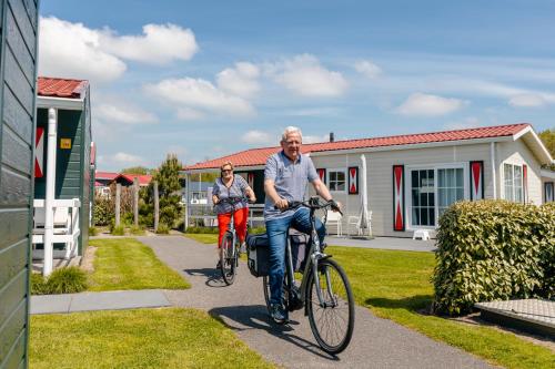 a man and woman riding bikes in front of a house at Strandcamping Valkenisse in Biggekerke