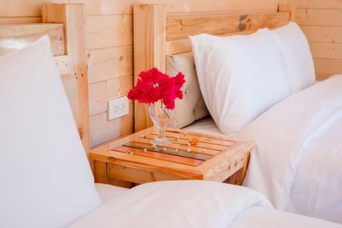 a vase with red flowers on a table between two beds at Bai Tu Long Mountain Resort in Hà Cái