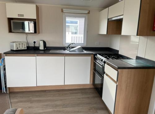 a kitchen with white cabinets and a stove top oven at Sycamores Caravan in Helston