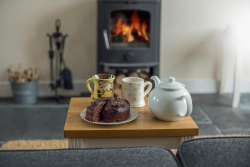 a table with a plate of chocolate cake and two cups at RURAL RETREAT WALES Indoor Hot Tub, Log Fire, Starry Skies, Woodland Walks in Llanfyrnach