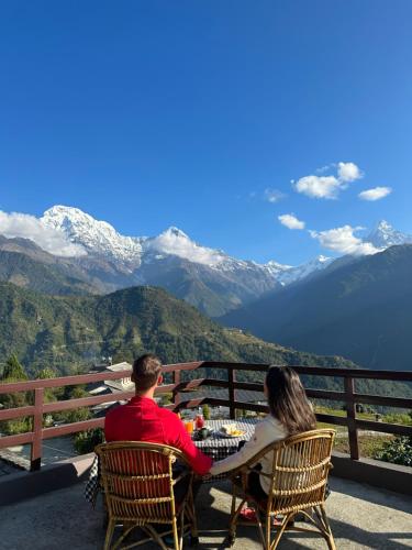 a man and woman sitting at a table with a view of mountains at Hill Top Lodge Ghandruk in Astam