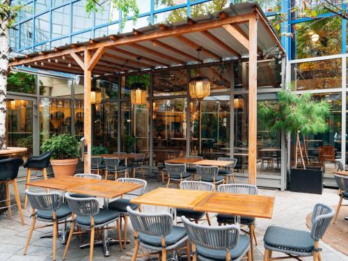 patio z drewnianymi stołami i krzesłami przed budynkiem w obiekcie Mercure Paris Val de Fontenay w mieście Fontenay-sous-Bois