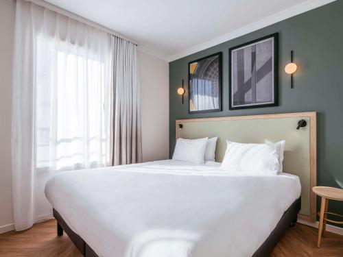 a large white bed in a room with a window at Aparthotel Adagio Paris Buttes Chaumont in Paris