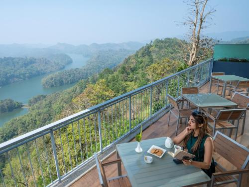 a woman sitting at a table on a balcony reading a book at Ragamaya Resort & Spa Munnar in Munnar