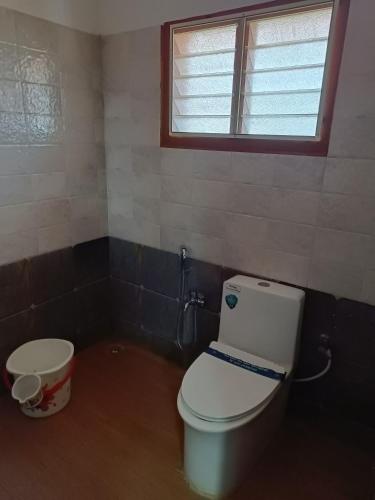 a bathroom with a toilet and a window and a bucket at VS HERITAGE INN in Vallam