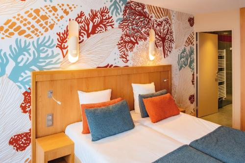 sypialnia z łóżkiem z pomarańczowymi i niebieskimi poduszkami w obiekcie Club Vacances Bleues Les Jardins De l'Atlantique w mieście Talmont-sur-Gironde