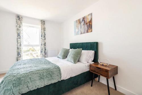 a bedroom with a bed with a green headboard and a table at Luxury Modern 2 Bed Apartment in Ebbsfleet - 20mins from London in Swanscombe