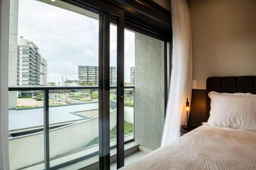 a bedroom with a bed and a large window at Loft 406 Parque Una + garagem in Pelotas