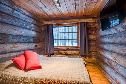 Dormitorio con cabaña de madera y cama con almohadas rojas en Villa Poronperä, en Kuusamo