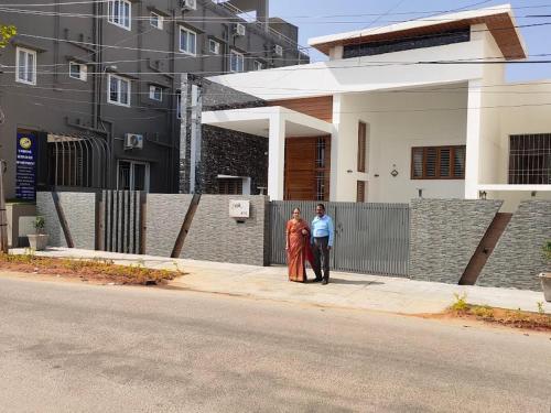 two people standing on a sidewalk in front of a house at Earth - Luxurious 5 BHK AC Villa at Mysore in Mysore