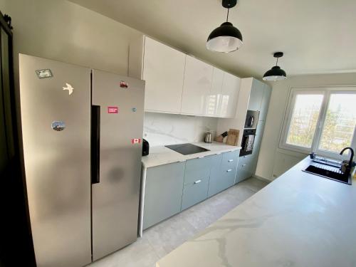 une cuisine avec un réfrigérateur en acier inoxydable et des armoires blanches dans l'établissement Bel appartement de 77m2 à Boulogne au pied du métro, à Boulogne-Billancourt