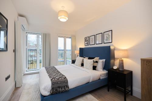 a bedroom with a blue and white bed and windows at The Wembley Park Gem - Lovely 2BDR Flat with Balcony in London