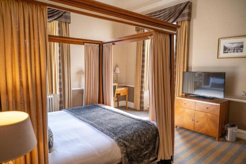 a bedroom with a canopy bed and a television at Dunkeld House Hotel in Dunkeld