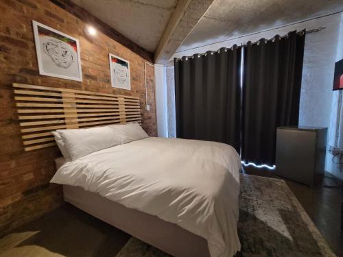 a bedroom with a white bed with a brick wall at Trendy apartments _ @ Craftsmanship on main in Johannesburg