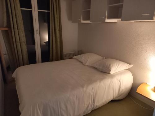 een bed met witte lakens en kussens in een kamer bij charmant appartement port de Dives sur mer in Dives-sur-Mer