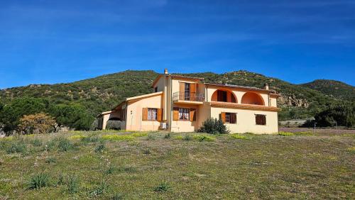 ein Haus auf einem Feld mit einem Berg im Hintergrund in der Unterkunft Villa Jolies in Viddalba