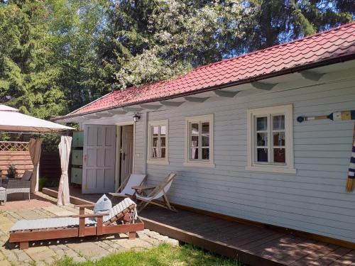 ein weißes Haus mit einer Veranda und einer Bank auf einer Terrasse in der Unterkunft Tulipanek - domek letniskowy z ogródkiem in Stegna
