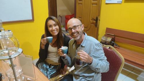 un homme et une femme assis à une table tenant des tasses dans l'établissement Pintu Biru Hostel, à Wamena