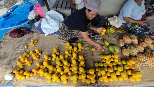 Uma mulher está ao lado de um monte de fruta. em Pintu Biru Hostel em Wamena