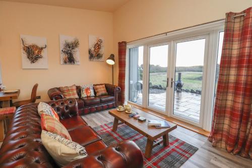 a living room with leather furniture and a large window at Red Squirrel in Dornoch