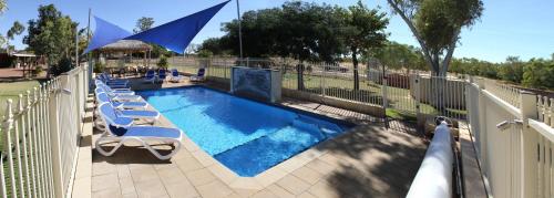 a swimming pool with lounge chairs next to a fence at Halls Creek Motel in Halls Creek
