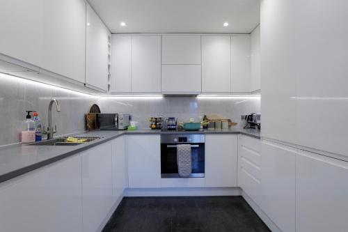 una cocina blanca con armarios y electrodomésticos blancos en Lovely Modern 1-Bed Flat in Kingston en Kingston upon Thames