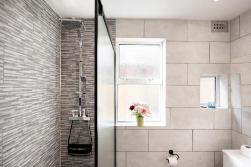 A Stylish Gem with King Beds and WiFi في لندن: حمام مع دش و مزهرية من الزهور في نافذة