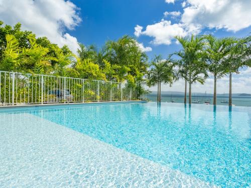 a swimming pool with palm trees and the ocean at B&B HOTEL Fort-de-France in Fort-de-France