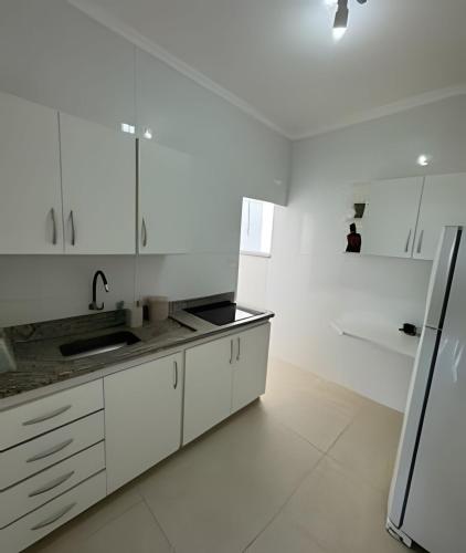a white kitchen with a sink and a refrigerator at Apartamento no Centro! in Franca