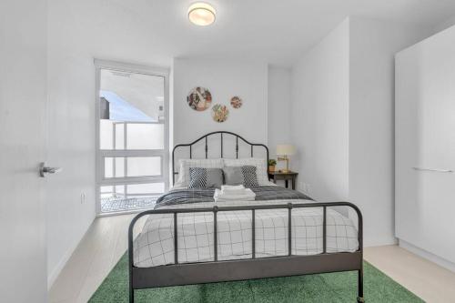 a white bedroom with a metal bed with a green rug at Modern Apt Near Downtown with Parking, AC & GYM in Vancouver