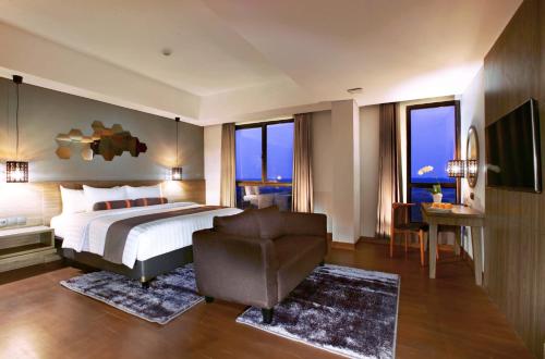 a bedroom with a bed and a chair and windows at Harper Purwakarta by ASTON in Purwakarta