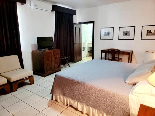 a bedroom with a bed and a chair and a television at Hotel Casa del Sol in Managua