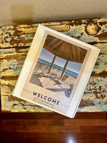 a book hanging on a wall with a picture of a beach at Salty Shenanigans in Kill Devil Hills