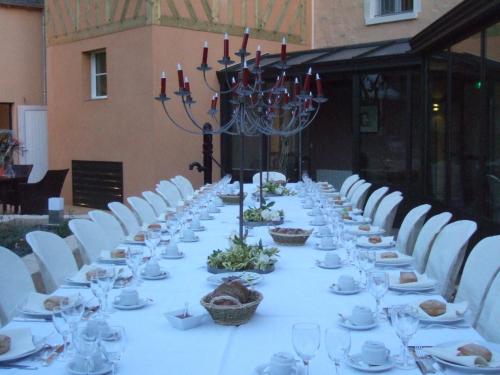 - une grande table avec des chaises blanches, des assiettes et des verres à vin dans l'établissement Hotel Le Saint Aubin, à Chevillé