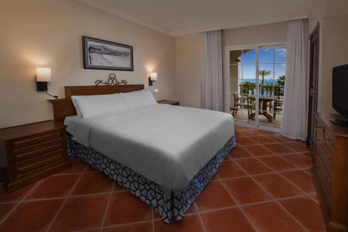 a bedroom with a bed and a television and a balcony at Marriott's Playa Andaluza in Estepona