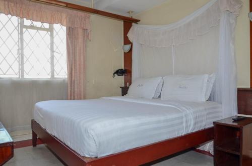 Una cama con sábanas blancas y almohadas en un dormitorio en Blue Hut Hotel en Nairobi